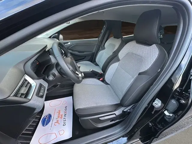 Intérieur avant droit de la Renault Clio V noire 2025, sièges tissu gris clair avec détails noirs, tableau de bord moderne.