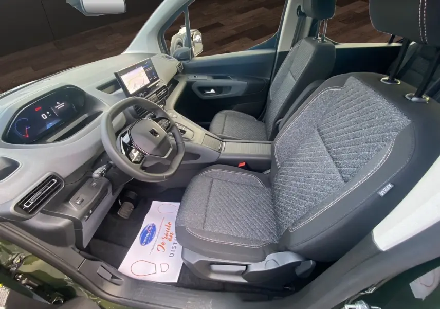 Vue intérieure côté conducteur du Peugeot Rifter 2025, sièges gris tissu et tableau de bord moderne avec écran tactile.