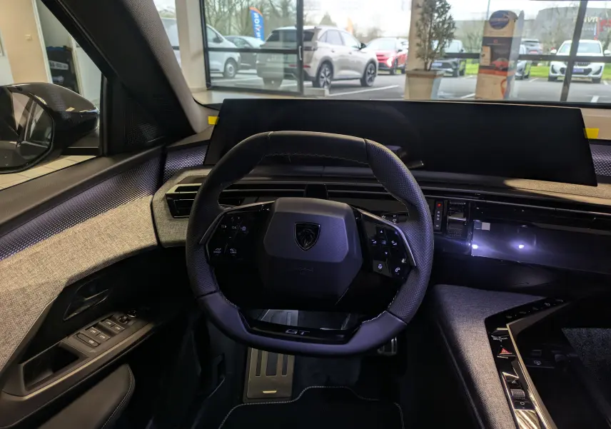 Vue intérieure centrée sur le volant compact du Peugeot 3008 gris titanium, avec tableau de bord numérique et finitions tissu grises.