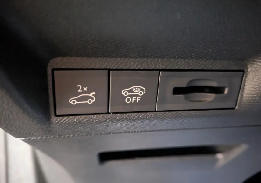 Détail intérieur montrant les boutons de commande d'ouverture du hayon et de désactivation d'alerte sur Peugeot 3008 gris titanium.