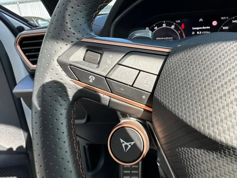 Gros plan sur le volant perforé noir et brun du CUPRA Formentor 1.5 eTSI Hybrid avec commandes intégrées et tableau de bord numérique.