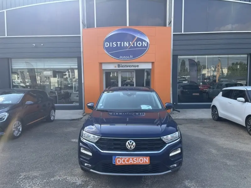 Volkswagen T-Roc bleu foncé vue de face, garée devant une concession avec panneau "Distinxion".