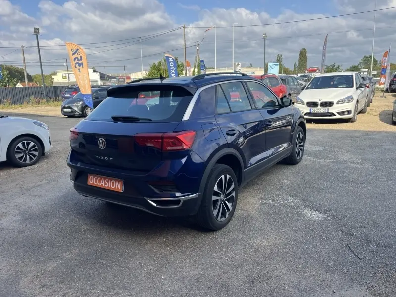 Vue 3/4 arrière droit d'un Volkswagen T-Roc bleu foncé avec jantes alliage, stationné en extérieur sur un parking.