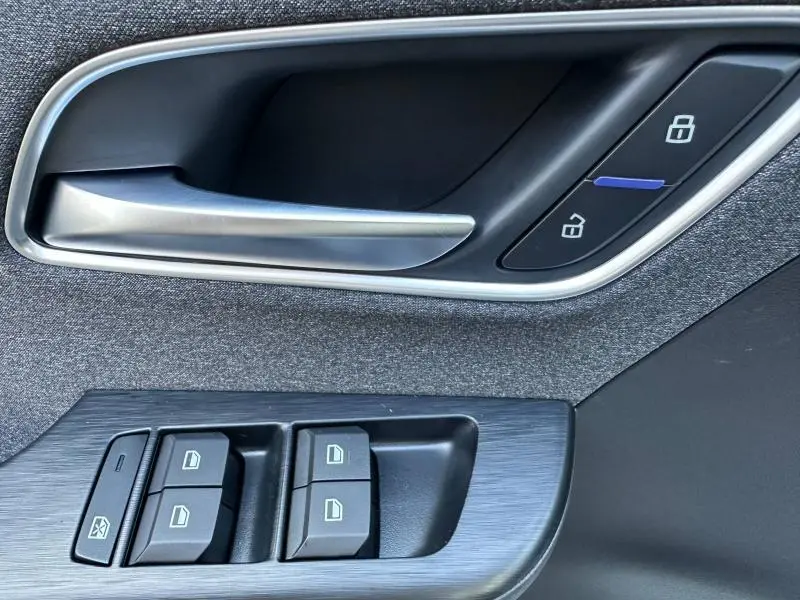 Gros plan sur la poignée intérieure et les commandes des vitres côté gauche du MG ZS Hybrid+ 2025 avec finition tissu noir.