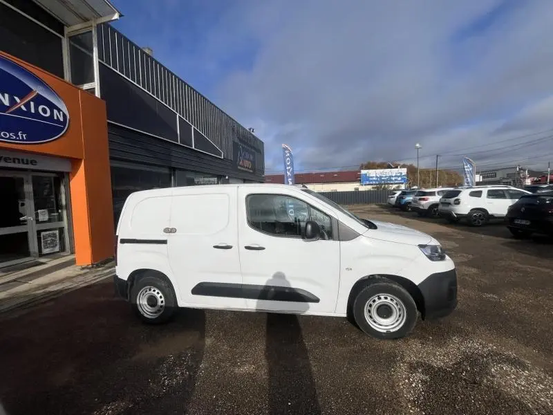 Profil côté gauche d'un utilitaire Citroën Berlingo Fourgon blanc Banquise stationné devant un bâtiment commercial.