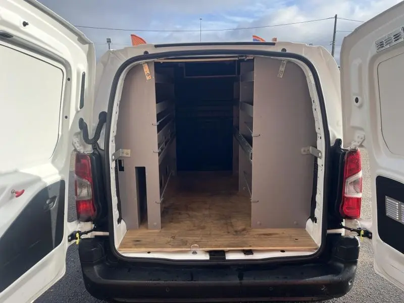Vue arrière ouverte du Citroën Berlingo Fourgon blanc Banquise montrant l'intérieur aménagé avec étagères grises et plancher bois.