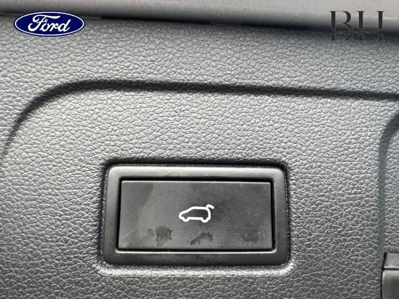 Bouton noir d'ouverture de coffre sur tableau de bord texturé, intérieur d'un Volkswagen Touran 2021.