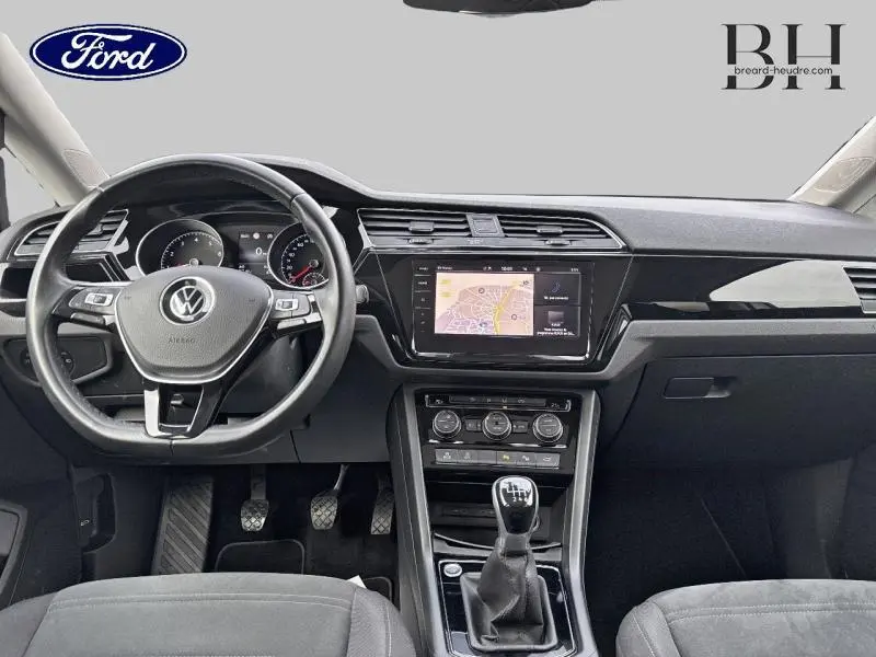 Vue intérieure avant du Volkswagen Touran 2021 avec tableau de bord noir, volant multifonction et écran tactile GPS.