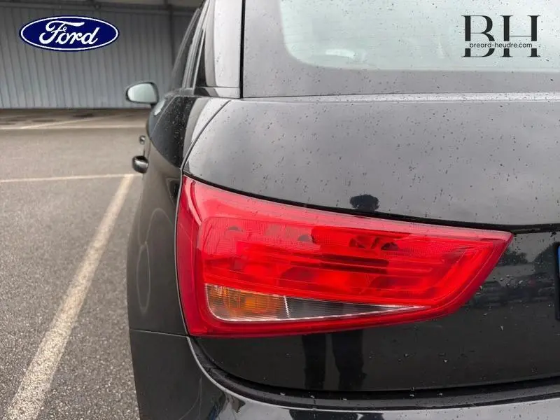 Gros plan sur le feu arrière droit d'une Audi A1 Sportback noire brillante sous la pluie.