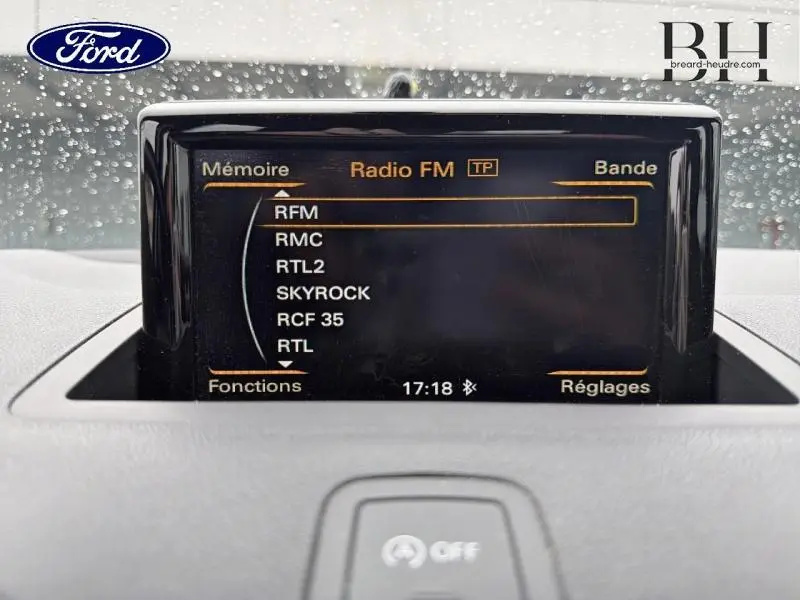 Écran multifonction noir affichant les stations radio FM dans l'habitacle d'une Audi A1 Sportback noire, vue de face.
