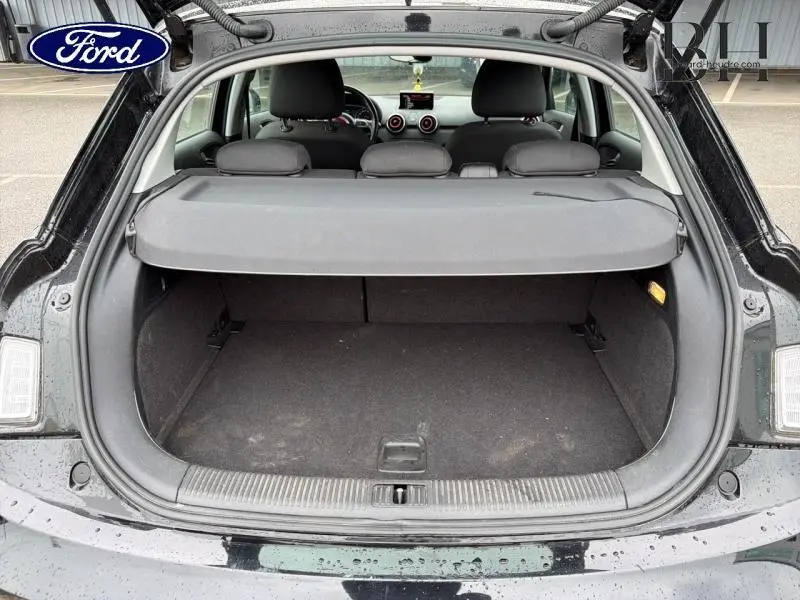 Coffre ouvert vu de l'arrière d'une Audi A1 Sportback noire brillante, montrant l'espace de chargement et la plage arrière.