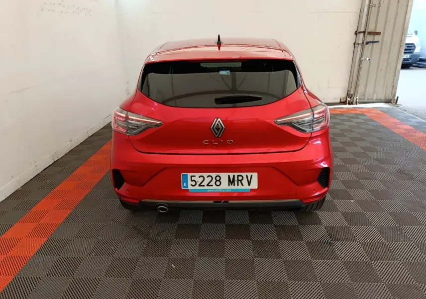 Vue arrière d'une Renault Clio rouge 2024 garée en intérieur avec feux arrière LED et échappement sport visible.
