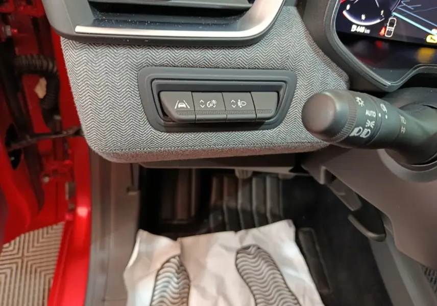 Vue intérieure côté conducteur de la Renault Clio Techno TCe 90 rouge 2024, avec commandes d’aide à la conduite et volant partiel.