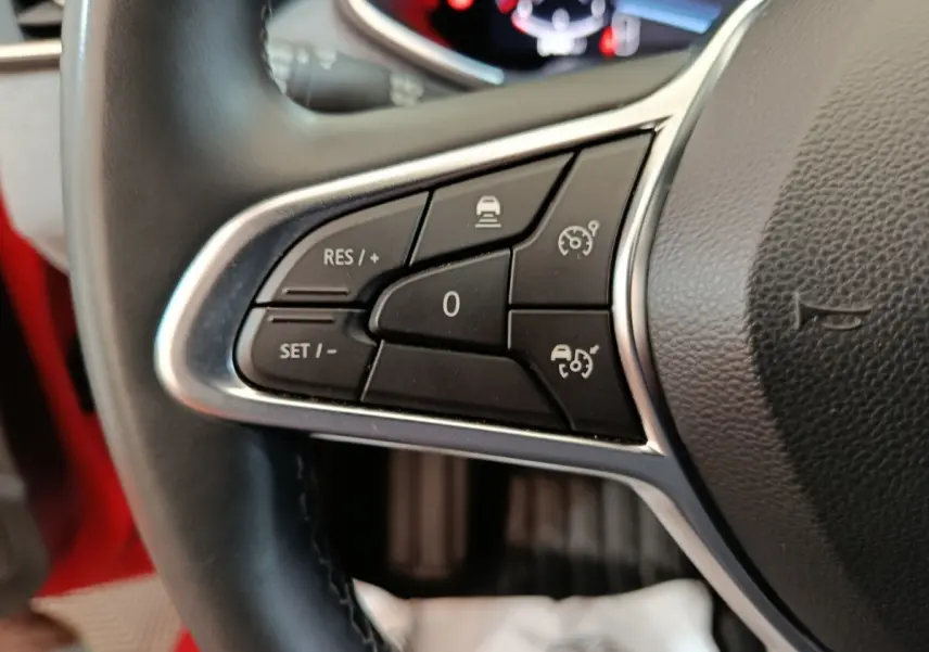 Gros plan sur les commandes du régulateur de vitesse au volant cuir d’une Renault Clio Techno rouge 2024.