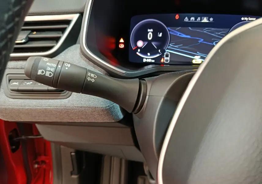 Vue rapprochée du combiné d'instruments numérique et du commodo gauche dans l'habitacle rouge de la Renault Clio Techno TCe 90 2024.
