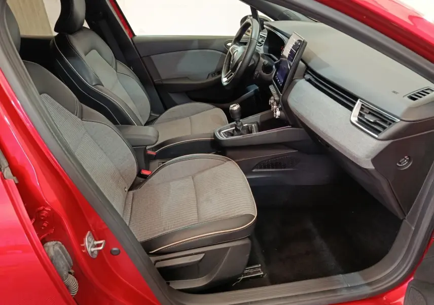 Vue intérieure côté conducteur de la Renault Clio Techno TCe 90 rouge 2024, avec sièges tissu et tableau de bord moderne.