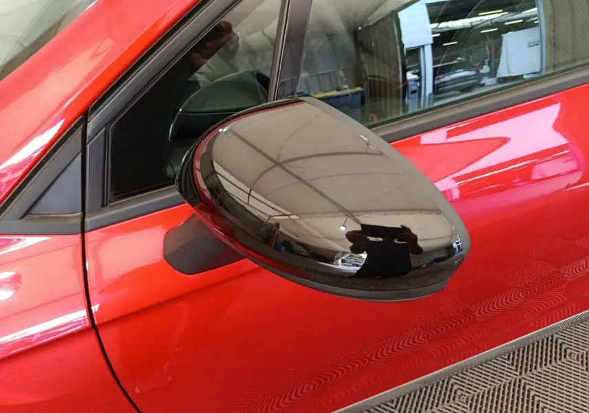 Gros plan sur le rétroviseur côté conducteur noir brillant d'une Renault Clio Techno TCe 90 rouge 2024.