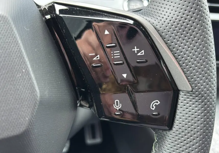 Gros plan sur les commandes noires brillantes au volant du Peugeot 3008 Hybrid 2026, côté gauche, avec boutons multifonctions.