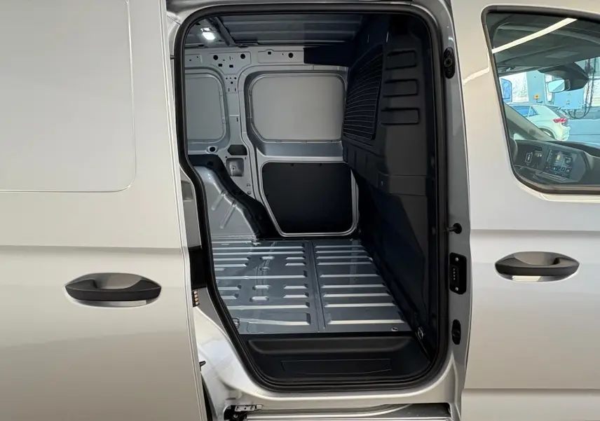Vue latérale droite du Volkswagen Caddy 2025 gris argent avec porte coulissante ouverte montrant l'espace de chargement vide.