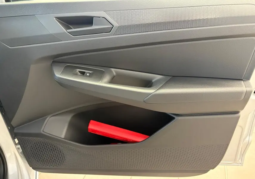 Intérieur de la porte côté gauche d'un Volkswagen Caddy gris argent 2025 avec rangement et triangle de signalisation rouge visible.