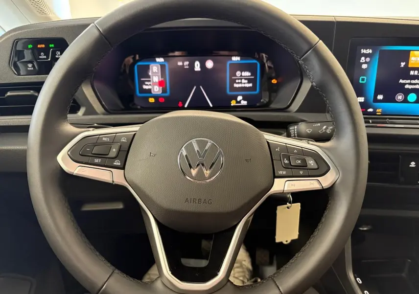 Vue rapprochée du volant noir du Volkswagen Caddy 2025 avec tableau de bord numérique et commandes intégrées.