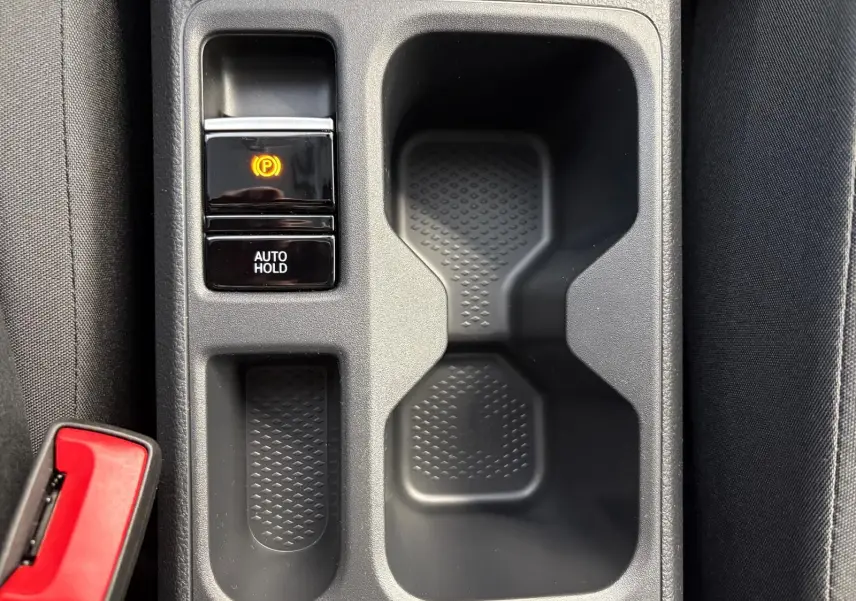 Gros plan sur la console centrale du Volkswagen Caddy 2025, avec bouton frein à main électronique et porte-gobelets noirs.