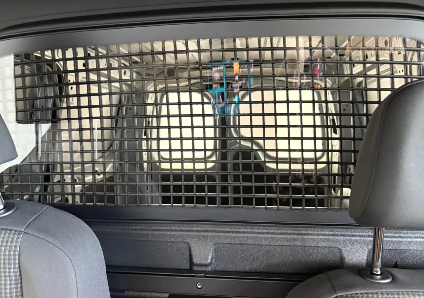 Vue intérieure arrière du Volkswagen Caddy gris argent 2025, montrant la grille de séparation entre cabine et espace de chargement.