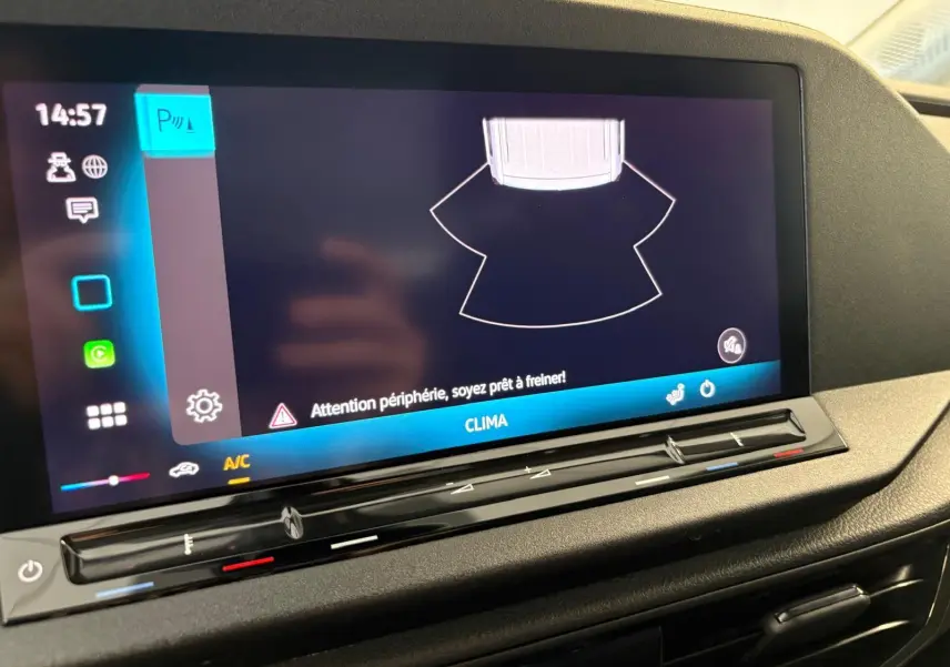Écran tactile du tableau de bord du Volkswagen Caddy 2025 gris argent, affichant l'alerte de périphérie et commandes climatisation.