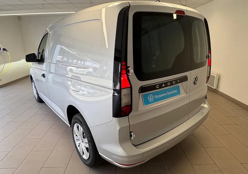 Vue 3/4 arrière droite du Volkswagen Caddy gris argent 2025, fourgon utilitaire avec portes arrière vitrées et feux verticaux.