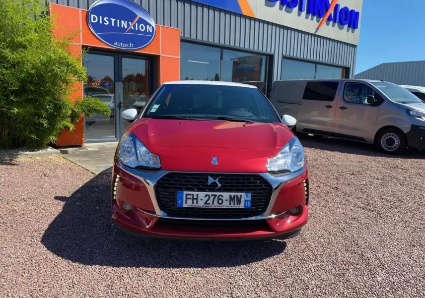 Vue de face d'une DS3 rouge au toit blanc, stationnée devant un bâtiment avec enseigne Distinxion.