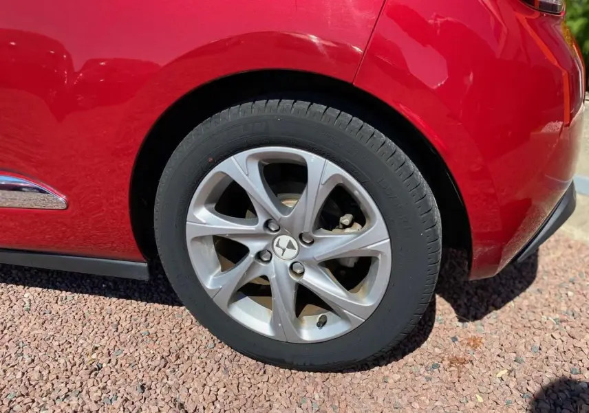 Gros plan sur la roue arrière droite argentée d'une DS3 rouge avec toit blanc, soulignant le design de la jante alliage.