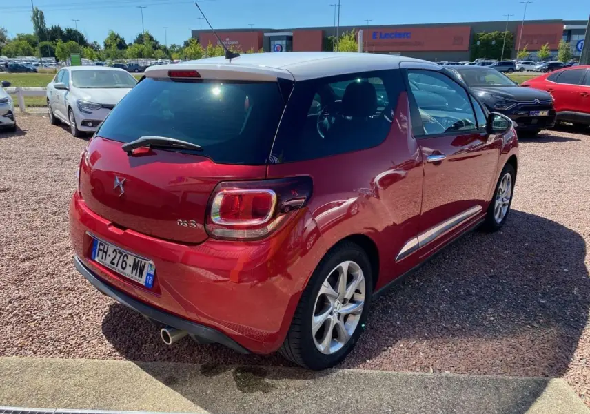Vue 3/4 arrière droite d'une DS3 rouge à toit blanc, avec jantes alliage et feu arrière carré distinctif.