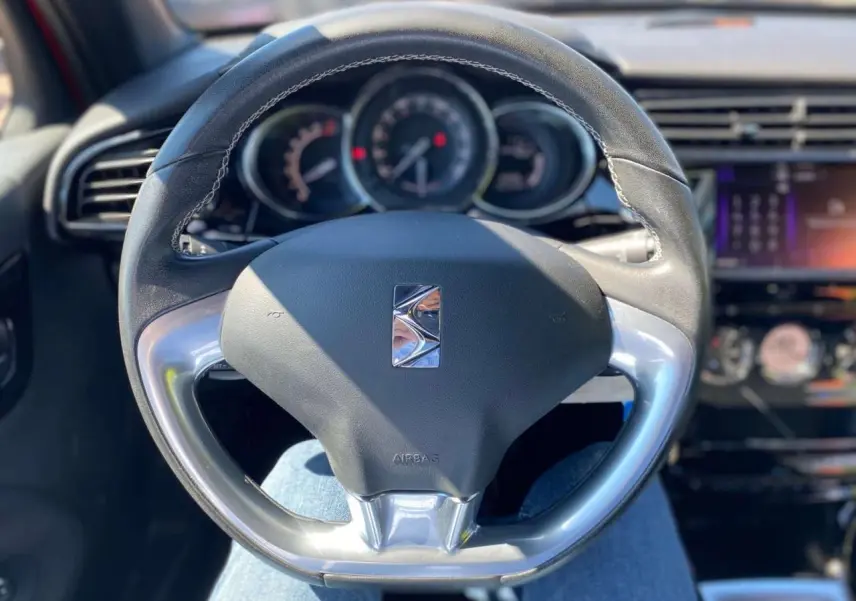 Vue rapprochée du volant DS3 2018 avec logo DS, tableau de bord et écran tactile en arrière-plan flou.