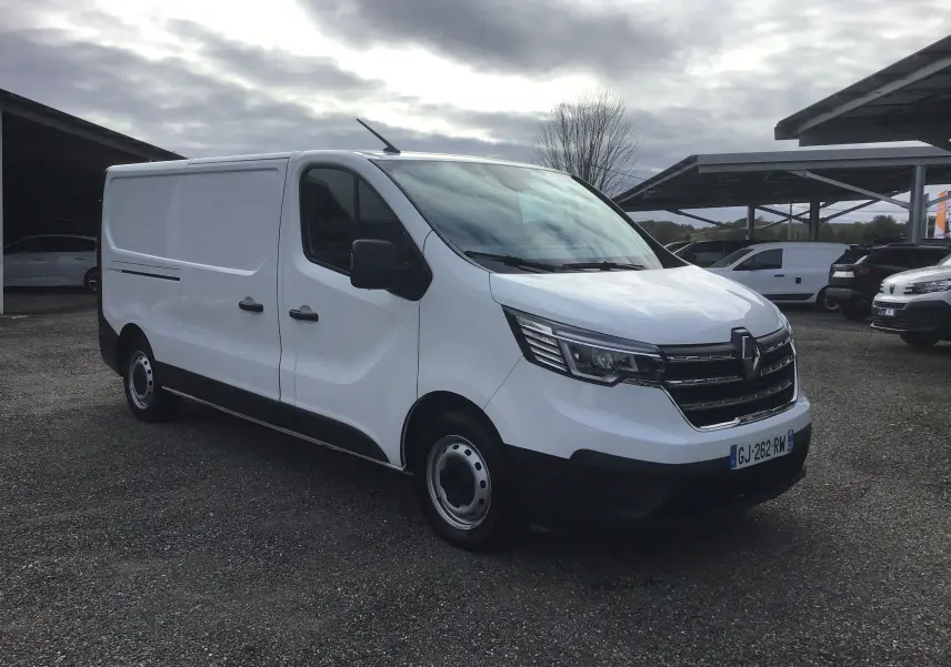 Renault Trafic Fourgon blanc vu en 3/4 avant droit sur parking, avec calandre noire et phares modernes.