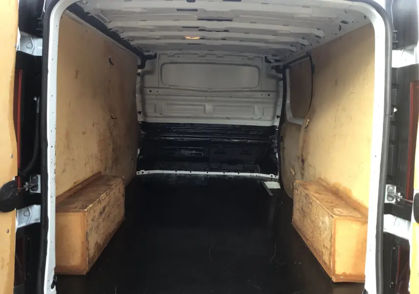 Intérieur du fourgon Renault Trafic blanc vu de l'arrière, avec parois en bois et plancher noir aménagé.