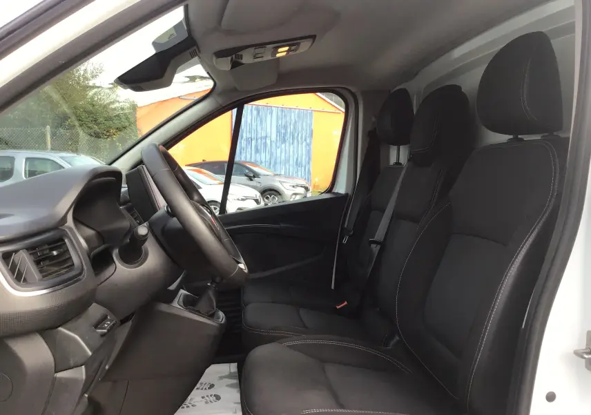 Vue intérieure côté conducteur du Renault Trafic Fourgon blanc 2022, montrant les sièges noirs et le volant.