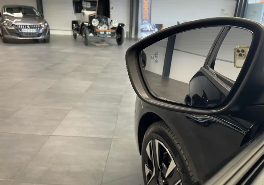 Rétroviseur côté droit d'une Peugeot 208 noire 2025 avec jante alliage bicolore et reflet intérieur showroom.