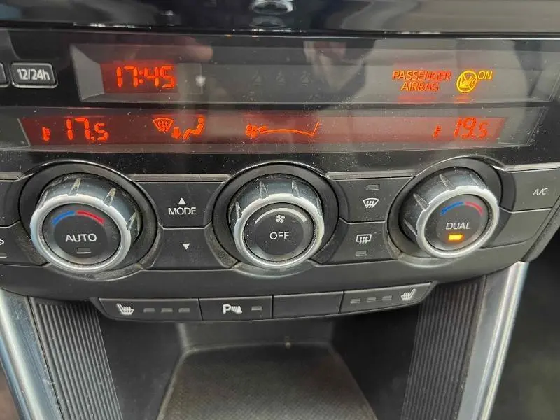 Vue rapprochée du tableau de bord du Mazda CX-5 2013 montrant les commandes de climatisation automatique bi-zone et affichage digital rouge.