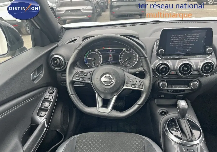 Vue intérieure centrée sur le poste de conduite du Nissan Juke 2024, volant cuir noir et console avec écran tactile.