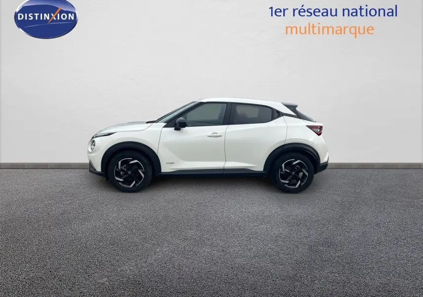 Vue de profil côté gauche d'un Nissan Juke blanc nacré 2024 avec jantes noires et toit contrasté noir.