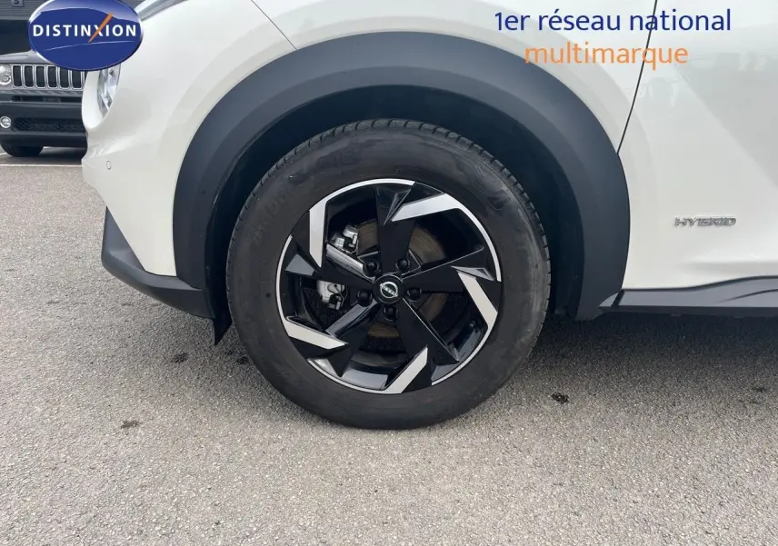 Gros plan sur la roue avant droite et la partie latérale blanche nacrée du Nissan Juke 1.6 HEV 143ch avec badge Hybrid visible.