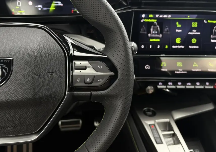 Vue rapprochée du volant perforé noir avec surpiqûres vert Adamite et écran tactile du Peugeot 308 SW Hybrid 2026.