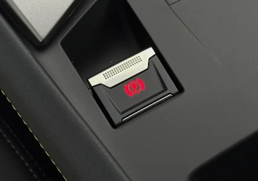 Gros plan sur le bouton de frein de parking électrique illuminé en rouge dans l'habitacle noir de la Peugeot 308 SW 2026.