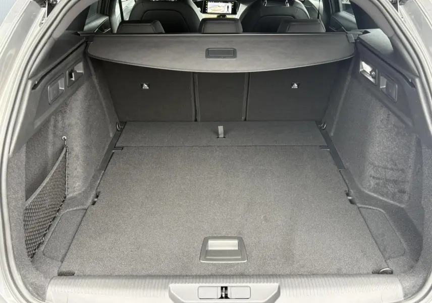 Coffre ouvert d’une Peugeot 308 SW gris Sélénium, vue arrière montrant un espace de chargement plat et un filet latéral.