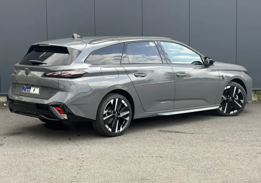 Vue 3/4 arrière droite d'une Peugeot 308 SW gris Sélénium avec jantes bi-ton et barres de toit noires.