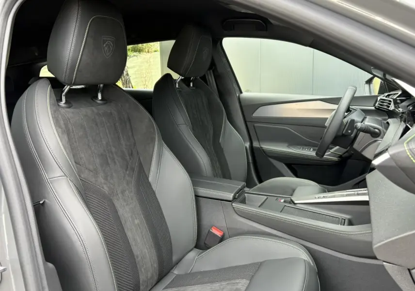 Vue intérieure côté conducteur de la Peugeot 308 SW 2026, sièges Alcantara noirs avec surpiqûres vert Adamite et volant compact cuir.