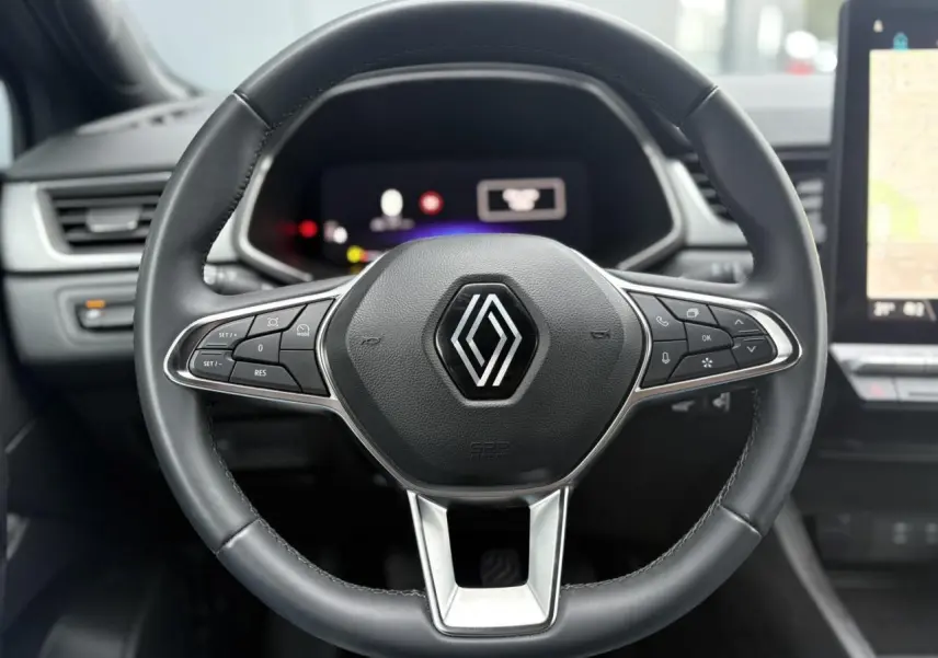 Vue rapprochée du volant noir du Renault Captur TCE 100 Techno 2025 avec commandes intégrées et tableau de bord numérique flou.