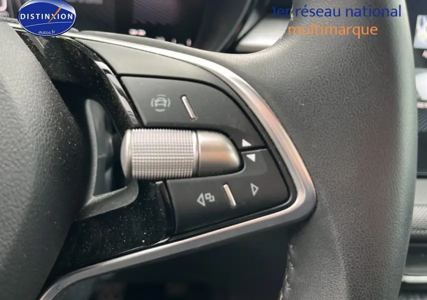 Gros plan sur les commandes multifonctions en métal et plastique noir du volant cuir côté gauche d’une Skoda Fabia noire.