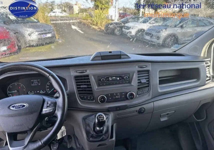 Vue intérieure côté conducteur du Ford Transit Custom blanc 2021, montrant le tableau de bord et la boîte manuelle.