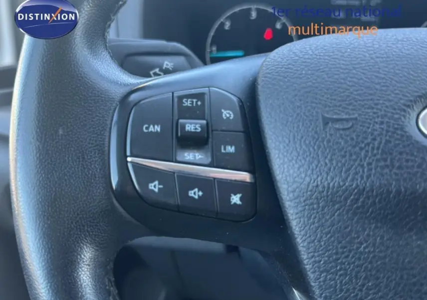Gros plan sur les commandes du volant cuir noir du Ford Transit Custom Fourgon blanc, avec régulateur de vitesse et contrôle audio.